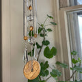 Decorative hanging mobile with beads and crystals in front of a window with plants.