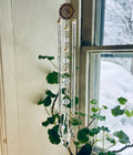 Decorative crystal hanging with green leaves in front of a window with snowy view