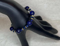 Blue beaded bracelet on a black mannequin hand against a textured gray background