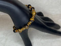 Bracelet with brown and gold beads on a black mannequin hand against a textured white background