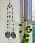 Decorative hanging crystal with floral designs in front of a window with a plant.