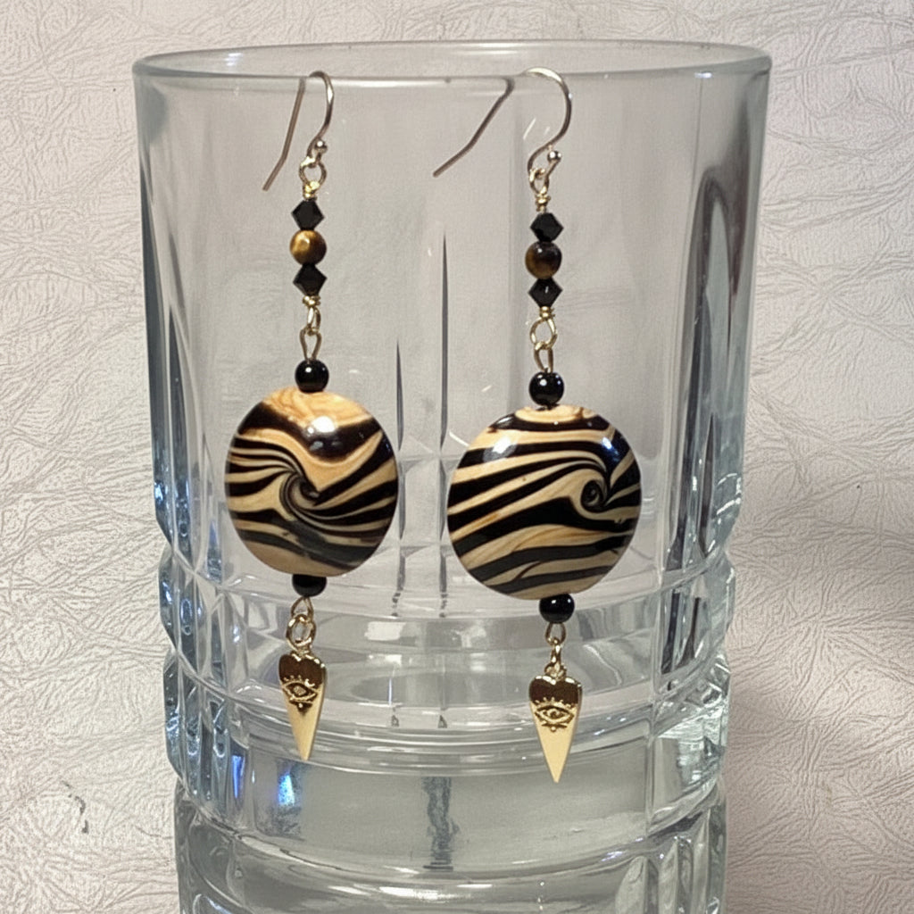 Pair of black and gold beaded earrings on a clear glass with a textured gray background