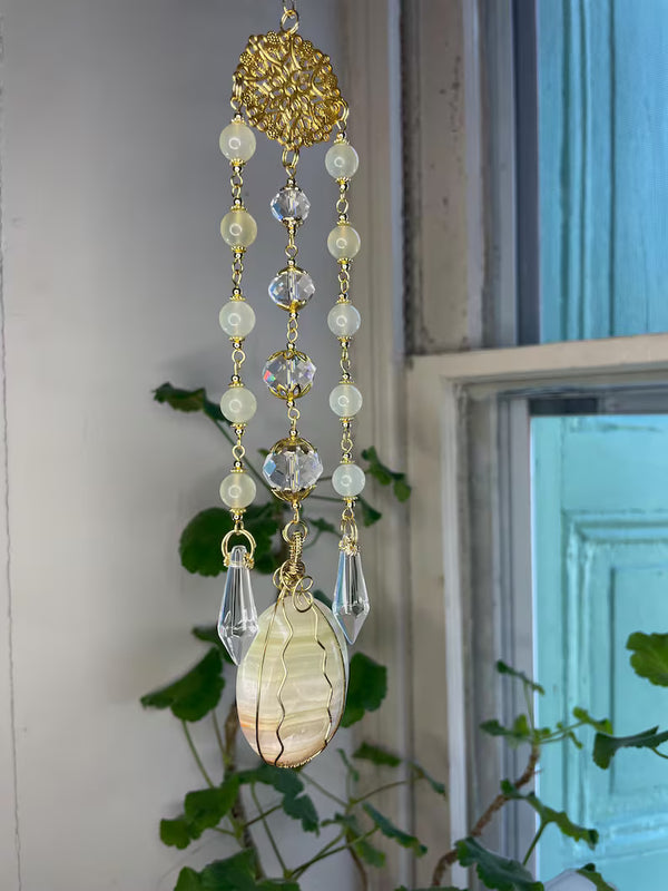 Decorative hanging ornament with beads and a teardrop-shaped crystal in front of a window.
