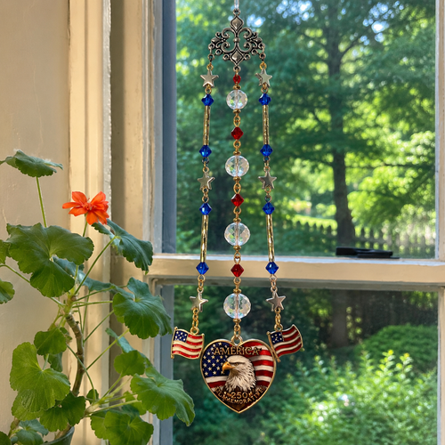 Handmade America 250 commemorative suncatcher featuring a Bald Eagle, American flag heart pendant, crystal prisms, and patriotic red, white, and blue accents hanging in a window.