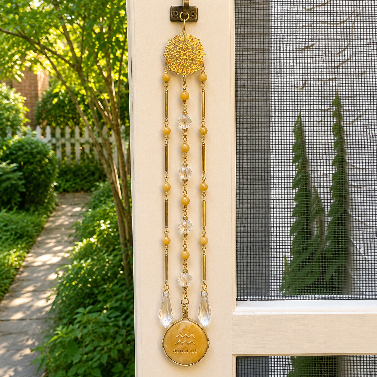 Handmade Aquarius zodiac suncatcher featuring a Yellow Aventurine pendant, crystal prisms, and gold-tone filigree accents hanging in a sunlit window.