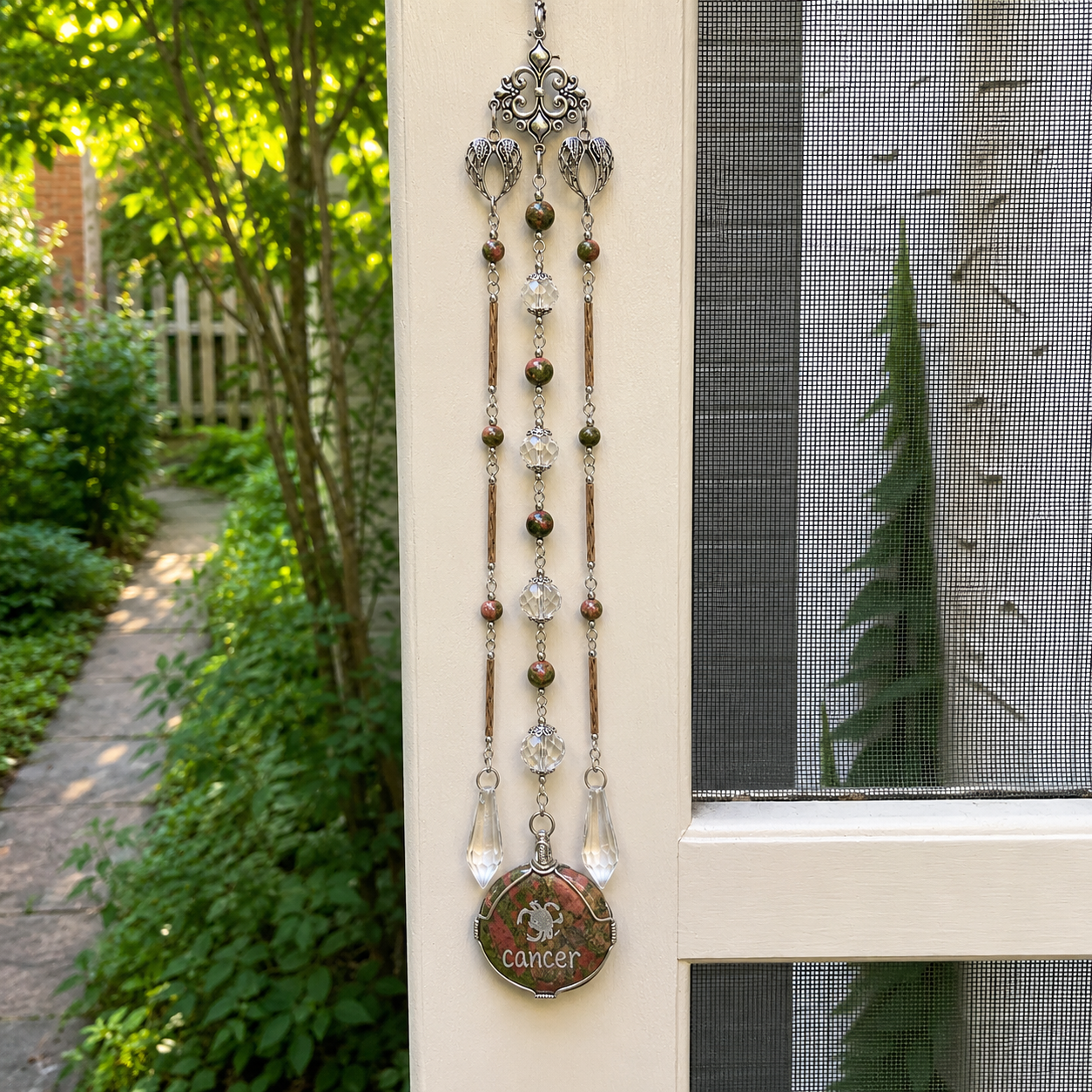 Handmade Cancer zodiac suncatcher featuring a Unakite pendant, crystal prisms, and silver angel wing accents hanging in a sunlit window.