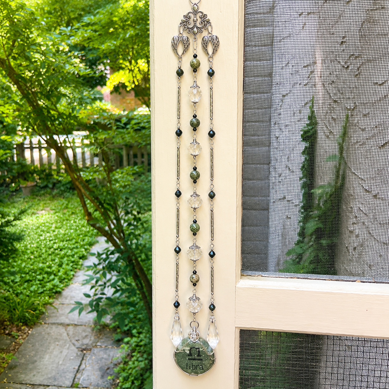 Handmade Libra zodiac suncatcher featuring a Serpentine gemstone pendant, crystal beads, and silver angel wing accents hanging in a sunlit window.