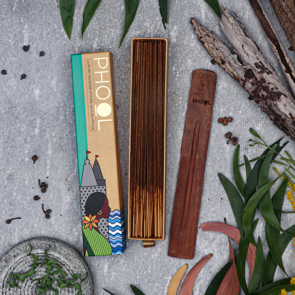A box of Phool Eucalyptus Incense Sticks alongside several sticks placed outside among leaves and wooden debris, suggesting a natural setting.