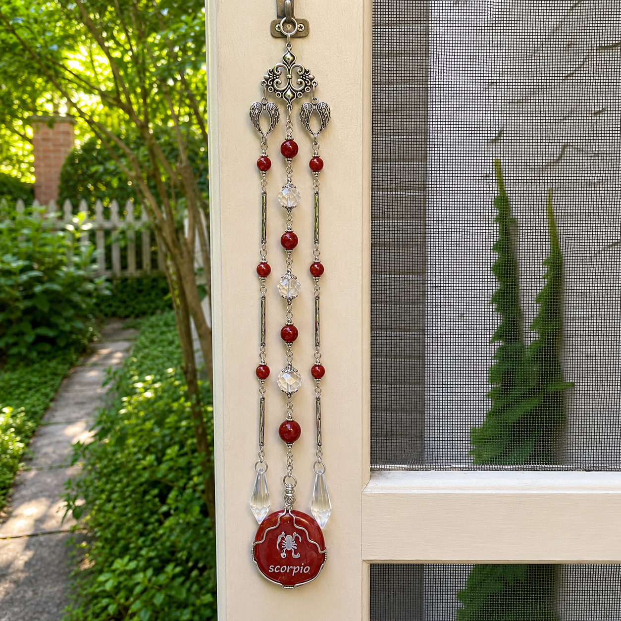 Handmade Scorpio zodiac suncatcher featuring a Red Jasper pendant, crystal prisms, and silver angel wing accents hanging in a sunlit window.