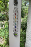 Decorative rainbow pendant hanging on a screen door with garden view