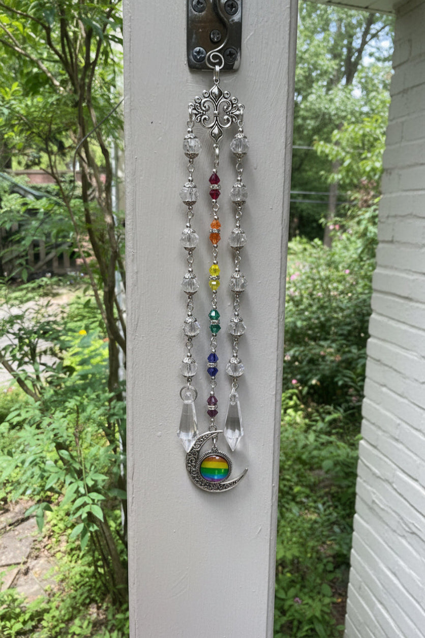 Decorative rainbow pendant hanging on a screen door with garden view