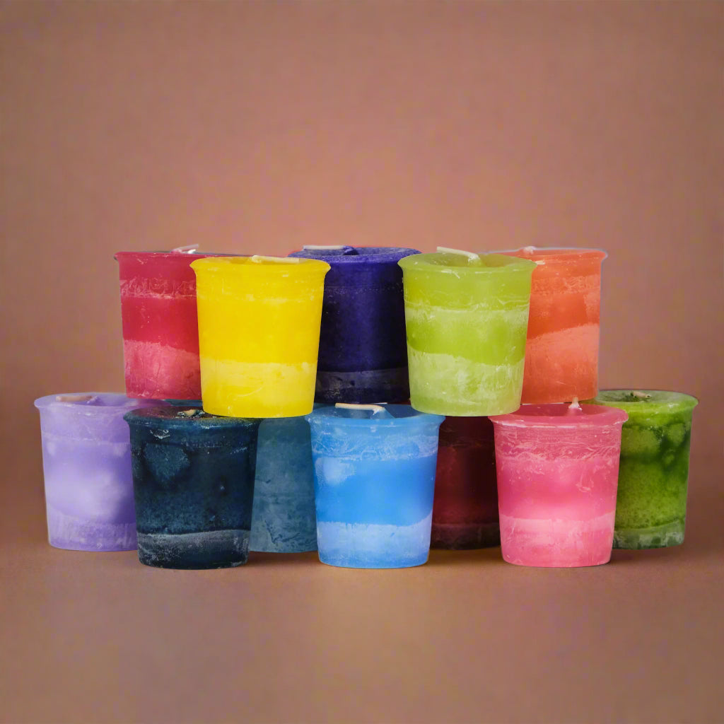 A collection of colorful votive candles, each in a different color, arranged in a semi-circle. They appear to be unlit and are placed on a white surface.