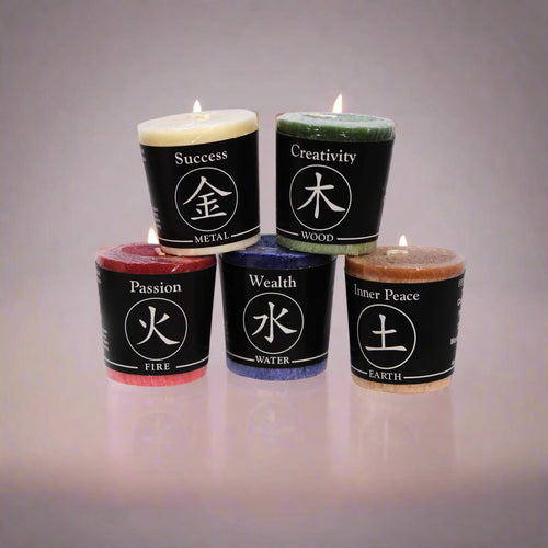 Five lit votive candles with colored labels indicating different qualities such as Success, Creativity, Passion, Wealth, and Inner Peace, arranged on a dark surface.