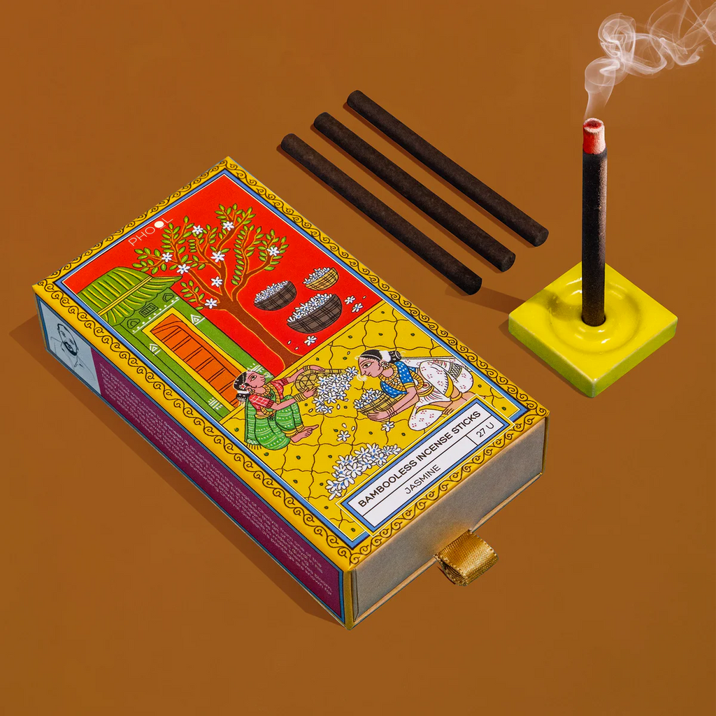 A box of Bambooless Jasmine Incense with incense sticks visible alongside a lit stick on a yellow holder, against a brown background.