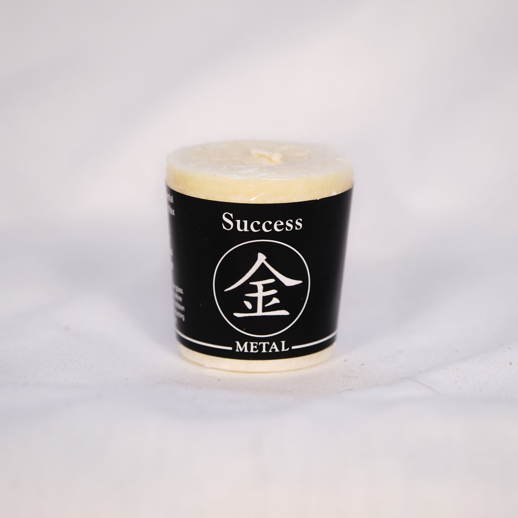 Five lit votive candles with colored labels indicating different qualities such as Success, Creativity, Passion, Wealth, and Inner Peace, arranged on a dark surface.